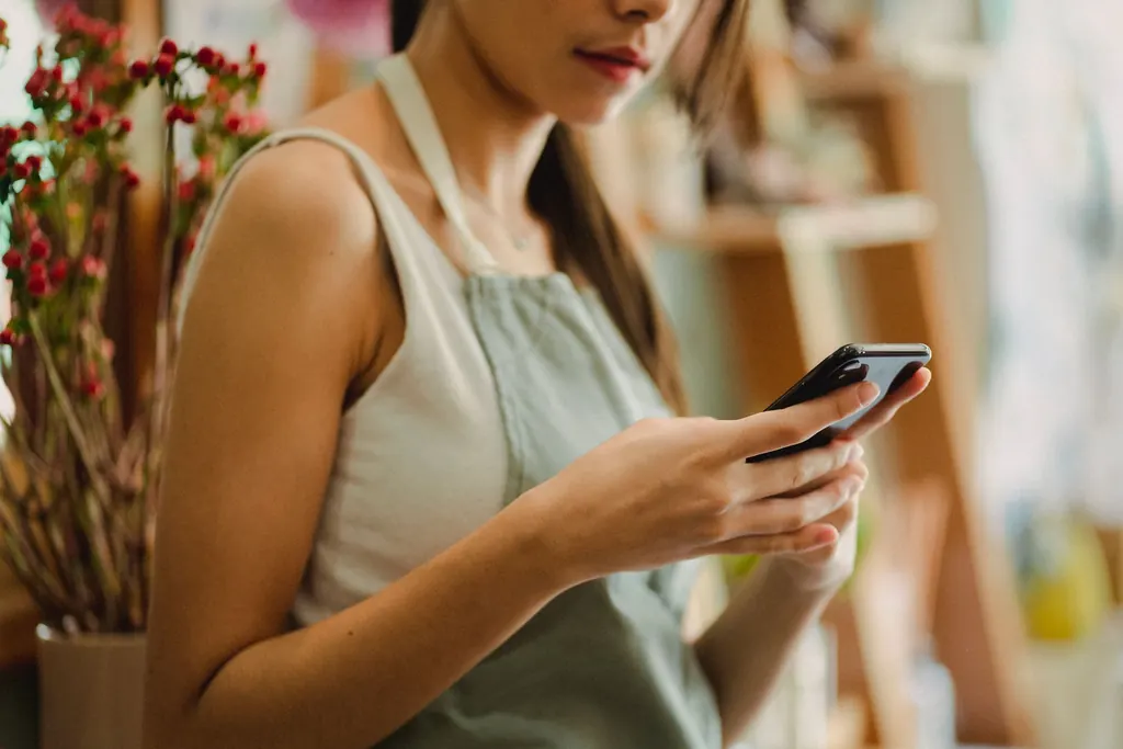 Manos de una florista con el celular, contestando un mensaje en su local